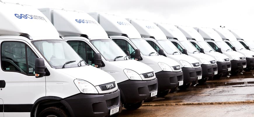 A row of white GeoAmey prisoner escort vans parked in a line